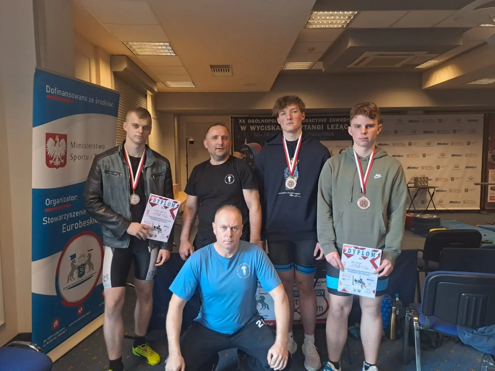 Zawodnicy wraz z trenerem prezentujący swoje osiągnięcia w postaci medalów po zmaganiach w zawodach.