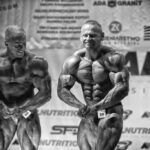 Zdjęcie prezentujące kulturystę podziwiającego sylwetkę konkurenta na scenie. Scena ma miejsce podczas zawodów Kamienna Rzeźba